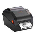 A black Bixolon thermal label printer with an orange accent button and a printed barcode label emerging from the front, shown on a solid white background.