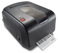 A Honeywell barcode label printer in matte black, shown with a white barcode label partially ejected from the front.