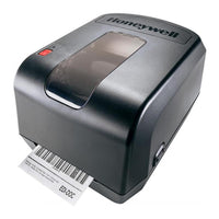 A Honeywell thermal label printer in matte black, shown with a barcode label partially ejected from the front. The printer features a glossy black top surface with the Honeywell logo, a translucent window on the lid, and a red power button.