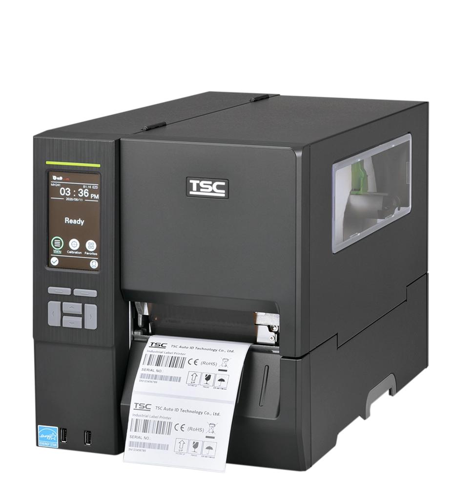 A TSC industrial barcode label printer with a dark gray and silver metallic body, showing a digital control screen on the front left and a white label sheet being printed and ejected from the front right.