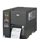 A TSC industrial barcode label printer with a dark gray and silver metallic body, showing a digital control screen on the front left and a white label sheet being printed and ejected from the front right.