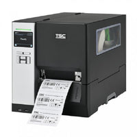 A TSC industrial barcode label printer with a dark gray and silver metallic body, showing a digital control screen on the front left and a white label sheet being printed and ejected from the front right.