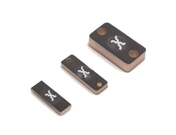 Three small rectangular black components with a white stylized 'X' logo and metallic copper-colored edges, arranged diagonally on a plain white background.