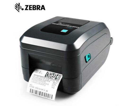 A Zebra QR-GT800 barcode scanner with a black and gray body, featuring a digital display screen and control buttons on top, with a white paper label partially ejected from the front, set against a plain white background.