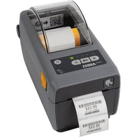 A Zebra Zebra ZD411 barcode scanner printer with a dark gray body, a white paper label emerging from the front, and a control panel with a small screen and buttons on top, set against a plain white background.