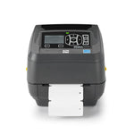 A Zebra QR-ZD500R barcode label printer in dark gray, shown with a white label sheet partially ejected from the front. The printer features a black control panel with a small LCD screen and directional buttons, set against a clean white background.